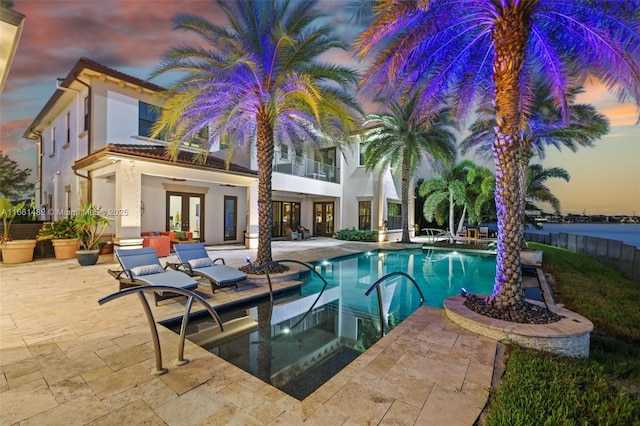 pool at dusk with a patio area, a jacuzzi, and french doors