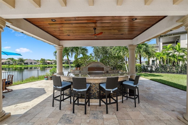 view of patio with a water view, exterior kitchen, a grill, ceiling fan, and an outdoor bar