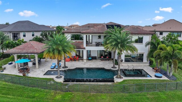 rear view of property featuring a patio, a balcony, a lawn, a pool with hot tub, and a gazebo