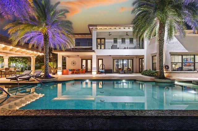 pool at dusk with ceiling fan and a patio area