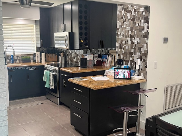 kitchen featuring sink, decorative backsplash, light stone countertops, appliances with stainless steel finishes, and light tile patterned flooring