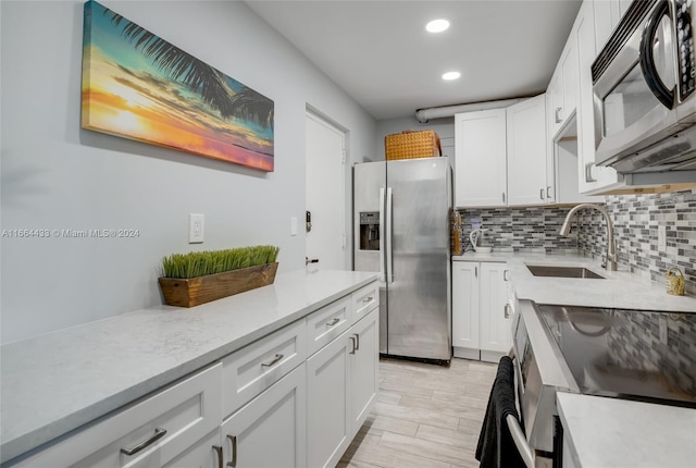 kitchen with appliances with stainless steel finishes, light stone counters, white cabinets, backsplash, and sink