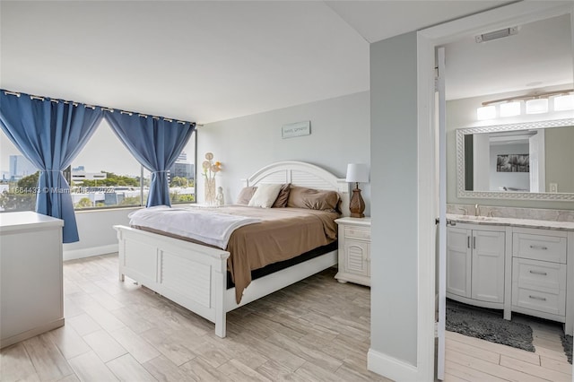 bedroom featuring connected bathroom, light hardwood / wood-style floors, and sink