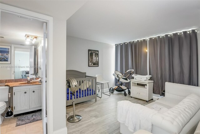 bedroom with connected bathroom, sink, and light hardwood / wood-style flooring