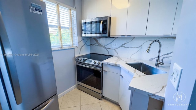 kitchen with stainless steel appliances, light stone counters, white cabinets, decorative backsplash, and sink