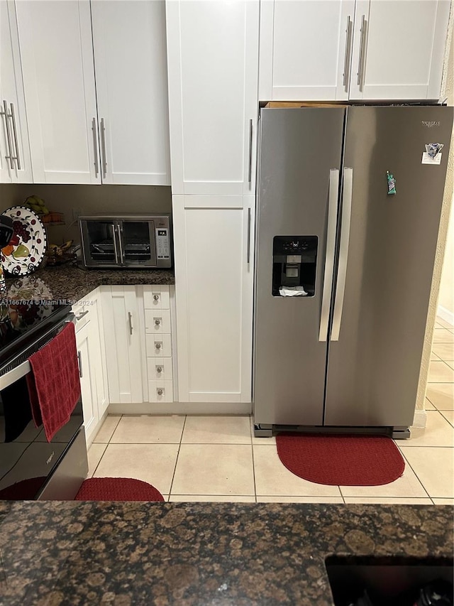 kitchen featuring appliances with stainless steel finishes, dark stone counters, light tile patterned floors, and white cabinets