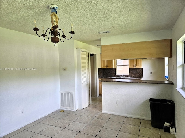 kitchen with light tile patterned floors, kitchen peninsula, a textured ceiling, backsplash, and a notable chandelier