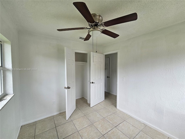 unfurnished bedroom featuring a textured ceiling, light tile patterned flooring, ceiling fan, and a closet