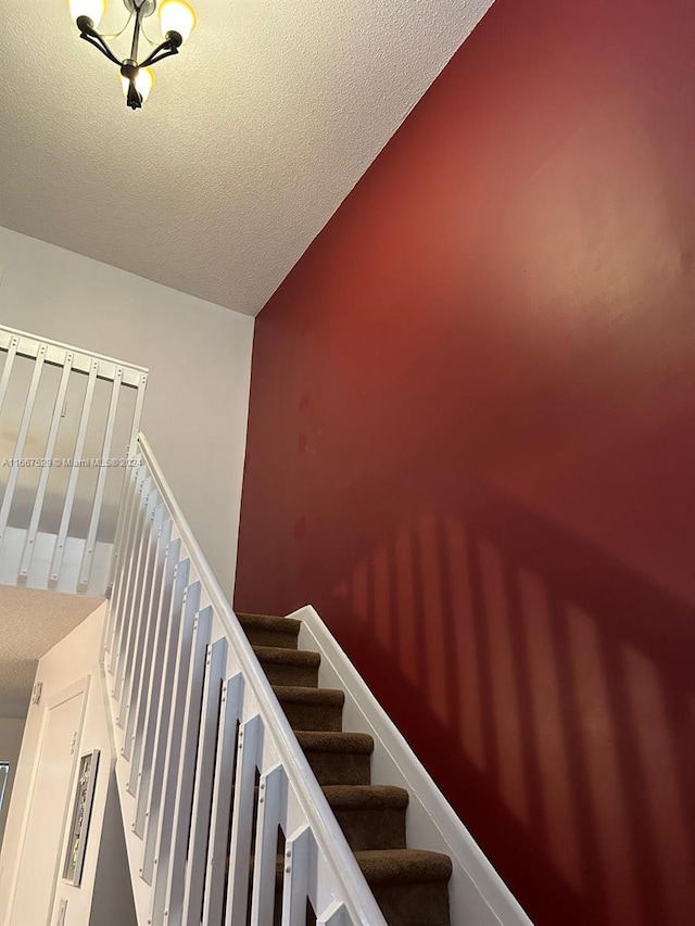 staircase featuring lofted ceiling, a chandelier, and a textured ceiling