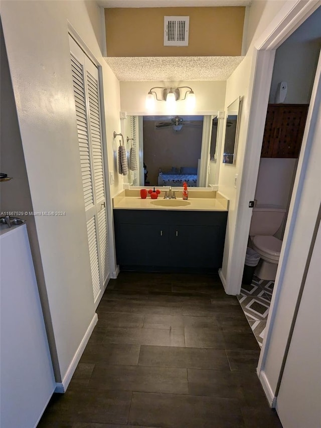 bathroom featuring wood-type flooring, vanity, toilet, and a textured ceiling