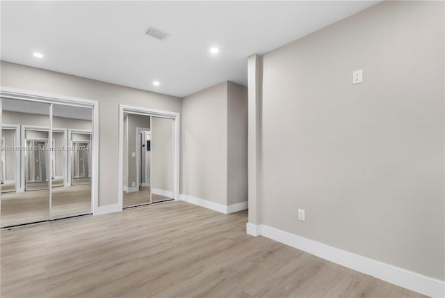 unfurnished bedroom featuring multiple closets and light hardwood / wood-style flooring