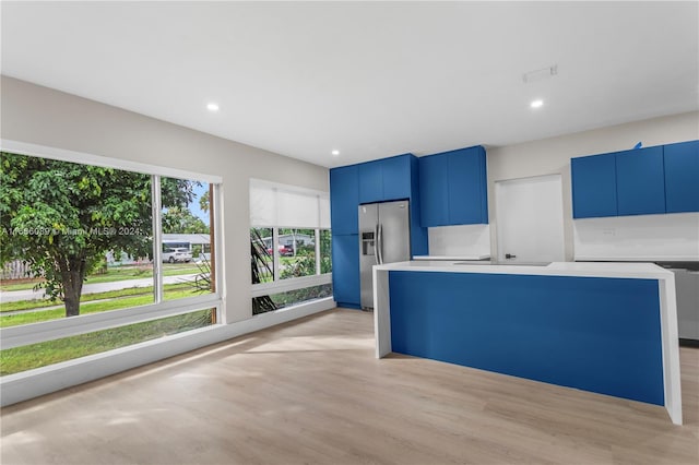 kitchen featuring light wood-type flooring, stainless steel refrigerator with ice dispenser, a kitchen island, and blue cabinetry