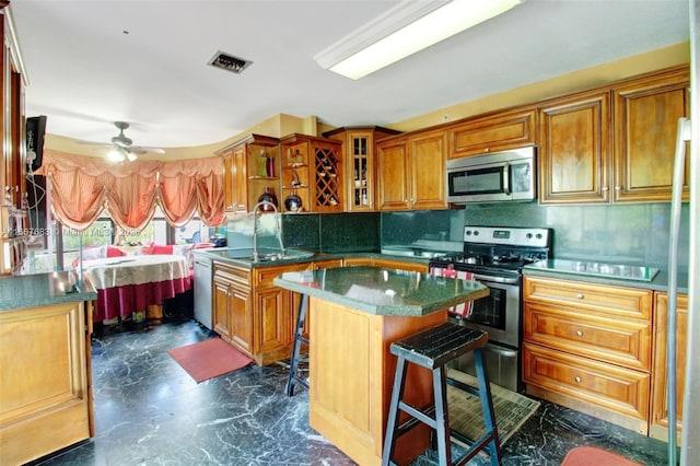 kitchen with a kitchen island, glass insert cabinets, appliances with stainless steel finishes, a breakfast bar, and a sink