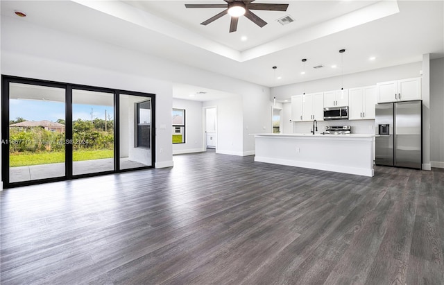 unfurnished living room featuring sink, ceiling fan, a tray ceiling, and dark hardwood / wood-style floors