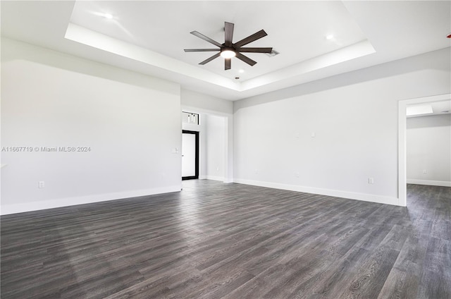 empty room with dark wood-type flooring, ceiling fan, and a raised ceiling