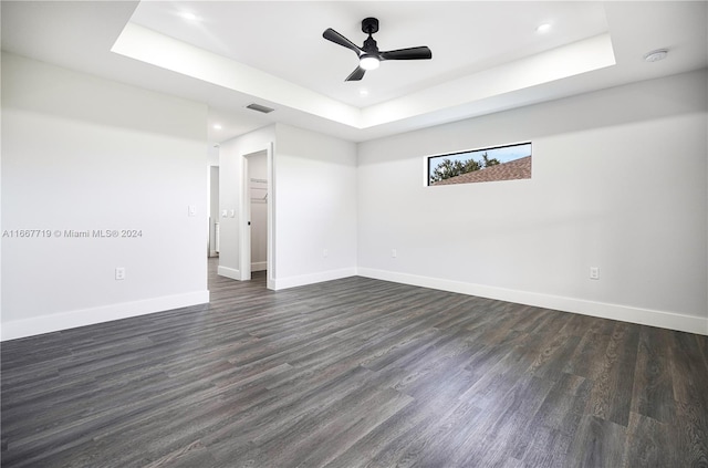 empty room featuring dark wood-type flooring, ceiling fan, and a tray ceiling