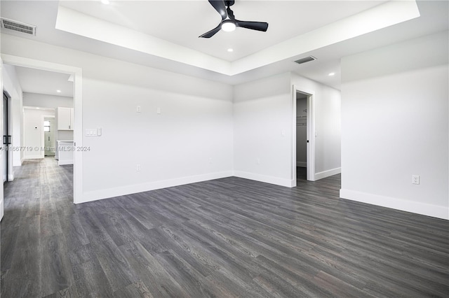 unfurnished room featuring a raised ceiling, dark hardwood / wood-style floors, and ceiling fan