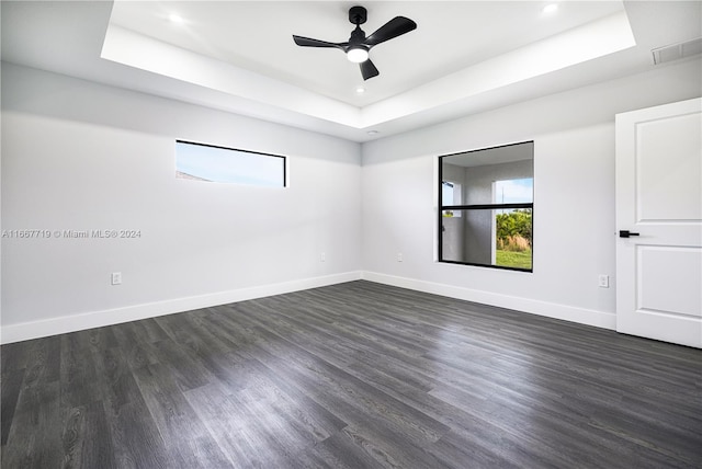 empty room with dark hardwood / wood-style floors, a tray ceiling, and ceiling fan