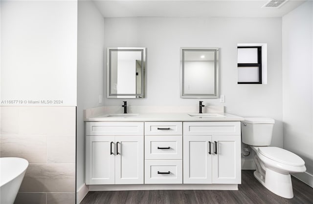 bathroom with hardwood / wood-style flooring, tile walls, toilet, a bath, and vanity