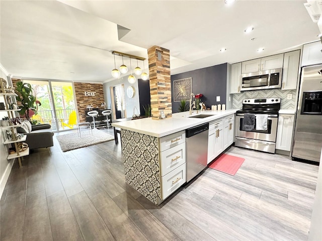 kitchen featuring a peninsula, a sink, light countertops, appliances with stainless steel finishes, and decorative backsplash