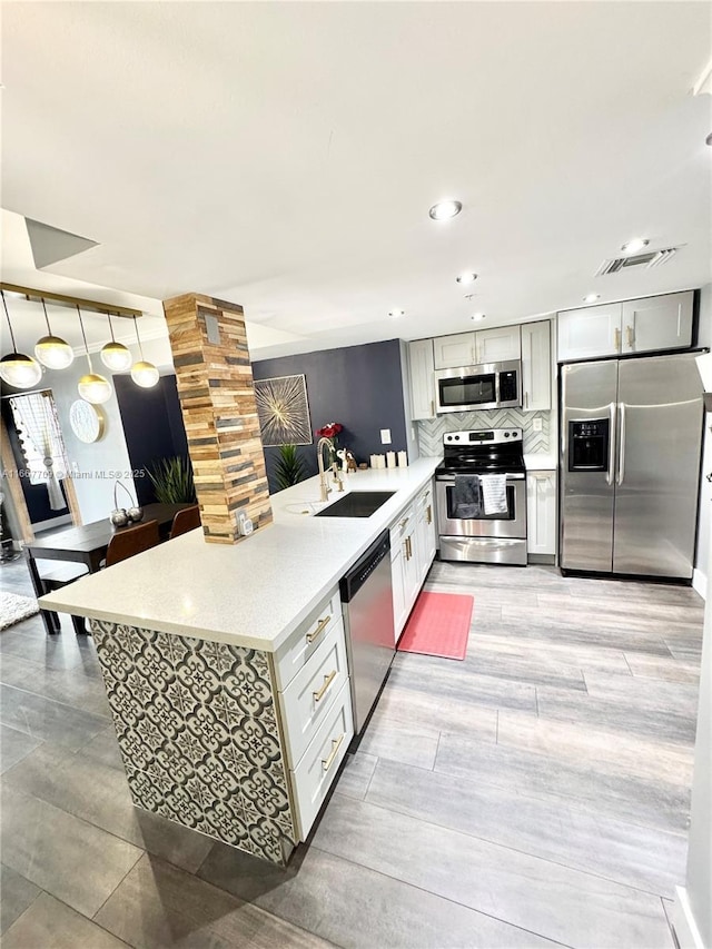 kitchen with visible vents, decorative backsplash, a peninsula, stainless steel appliances, and a sink