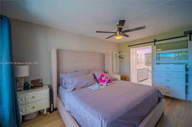 bedroom with a barn door, ceiling fan, light hardwood / wood-style flooring, and ensuite bath