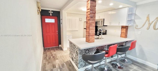 kitchen featuring crown molding, stainless steel appliances, white cabinetry, hardwood / wood-style floors, and decorative columns