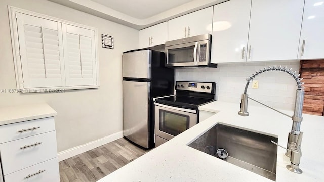 kitchen featuring light hardwood / wood-style floors, white cabinets, decorative backsplash, sink, and appliances with stainless steel finishes