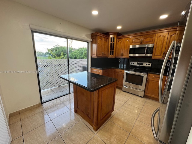 kitchen featuring dark stone counters, a center island, light tile patterned floors, appliances with stainless steel finishes, and tasteful backsplash