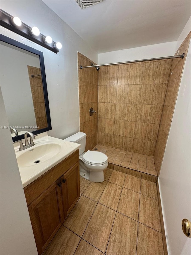 bathroom featuring vanity, a tile shower, and toilet