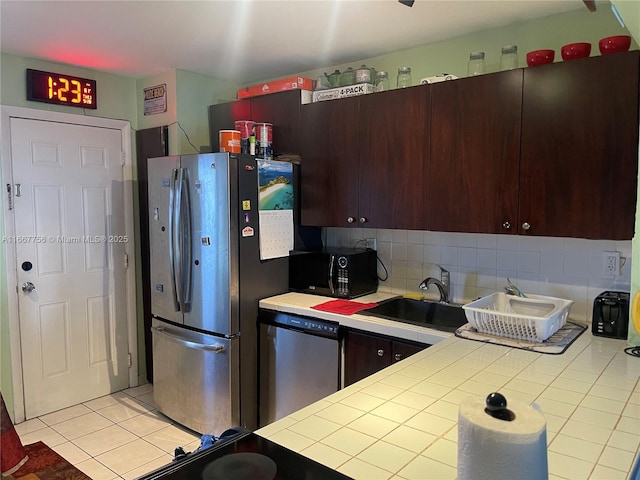 kitchen with sink, appliances with stainless steel finishes, backsplash, dark brown cabinets, and tile countertops