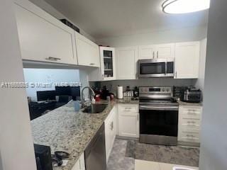 kitchen featuring appliances with stainless steel finishes, light stone countertops, sink, and white cabinets