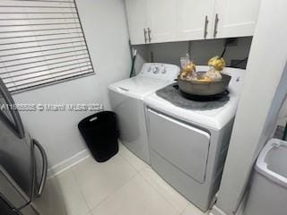 clothes washing area featuring cabinets, light tile patterned floors, and washing machine and dryer