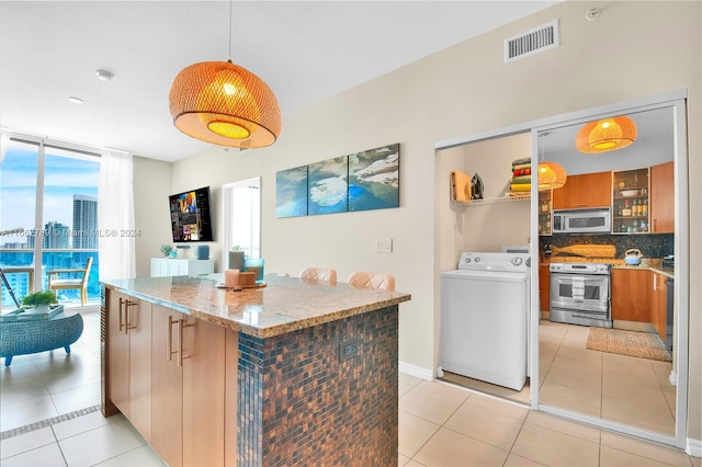 kitchen featuring appliances with stainless steel finishes, hanging light fixtures, decorative backsplash, light stone counters, and washer / dryer