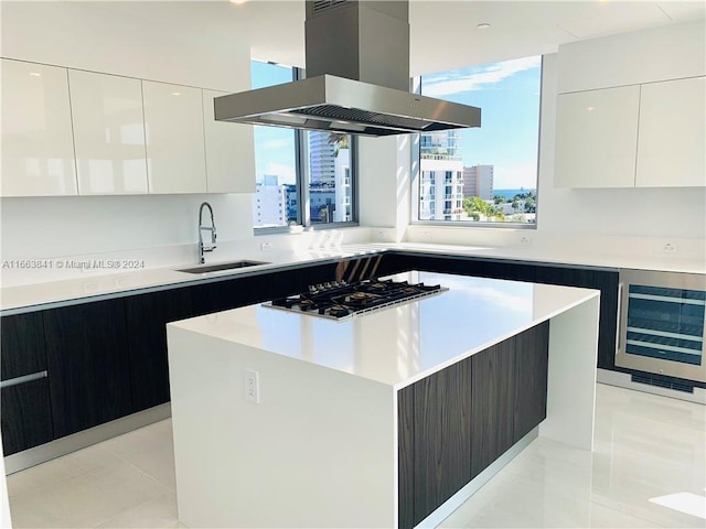 kitchen featuring sink, a kitchen island, white cabinetry, island exhaust hood, and stainless steel gas cooktop