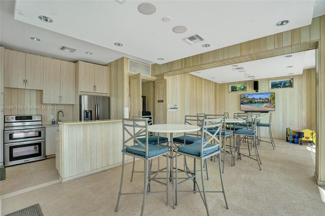 interior space with wood walls, a center island, light brown cabinets, and appliances with stainless steel finishes