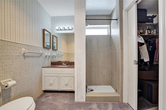 bathroom with tiled shower, vanity, toilet, and tile walls