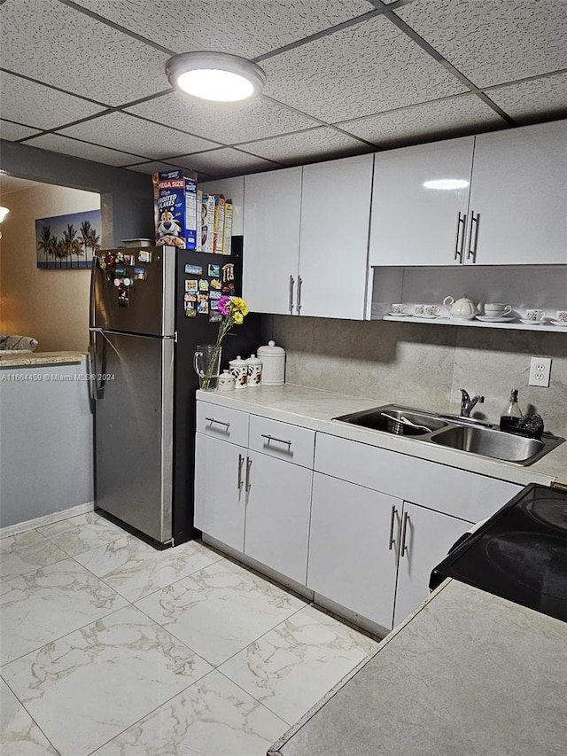 kitchen with a drop ceiling, stainless steel fridge, sink, and white cabinetry