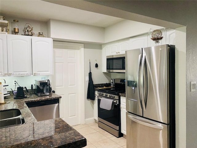 kitchen with dark stone countertops, light tile patterned flooring, white cabinets, stainless steel appliances, and sink