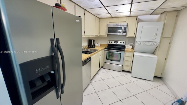 kitchen featuring light tile patterned floors, sink, cream cabinets, stacked washer / dryer, and stainless steel appliances