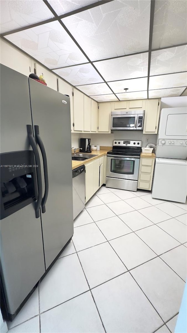 kitchen with stacked washer / drying machine, light tile patterned flooring, sink, cream cabinetry, and stainless steel appliances