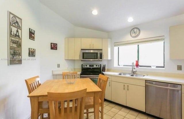 kitchen featuring appliances with stainless steel finishes, cream cabinetry, vaulted ceiling, light tile patterned floors, and sink