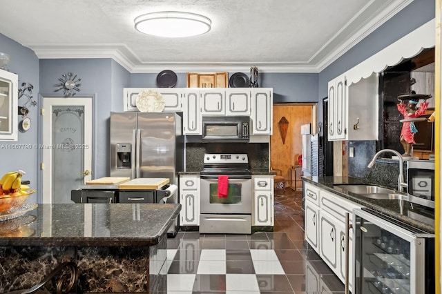 kitchen featuring beverage cooler, stainless steel appliances, a sink, white cabinetry, and backsplash