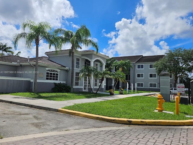 mediterranean / spanish-style home with a front yard, a tile roof, and stucco siding