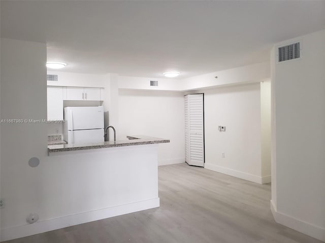 kitchen with kitchen peninsula, light hardwood / wood-style flooring, stone counters, white cabinetry, and white fridge