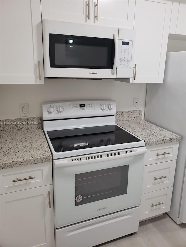 kitchen featuring light stone counters, white cabinets, light hardwood / wood-style flooring, and white appliances