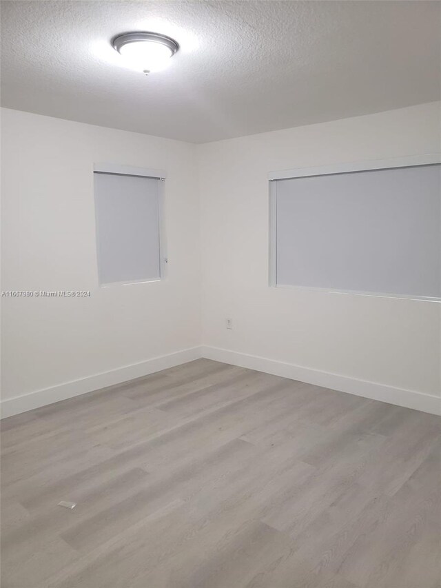 unfurnished room featuring a textured ceiling, wood finished floors, and baseboards