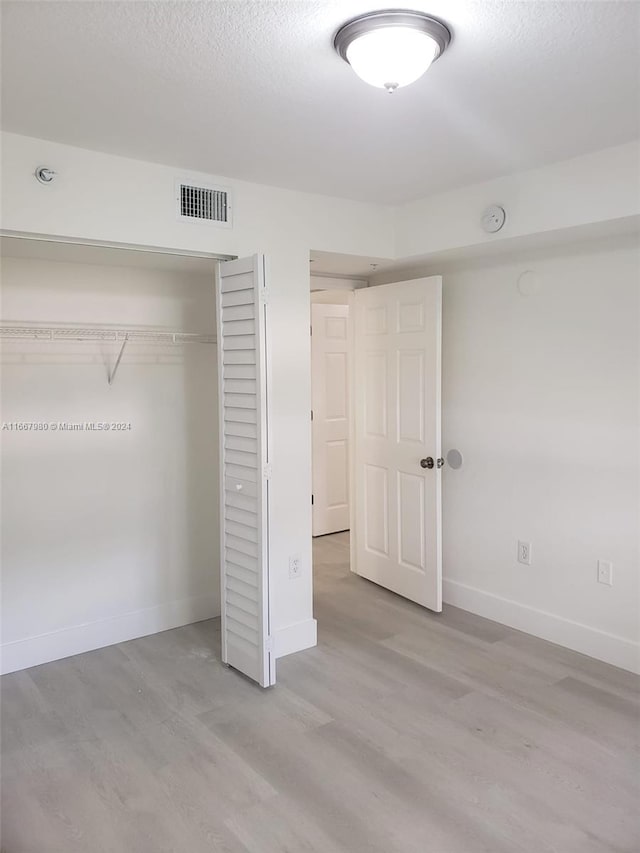 unfurnished bedroom featuring a textured ceiling, a closet, and light hardwood / wood-style floors