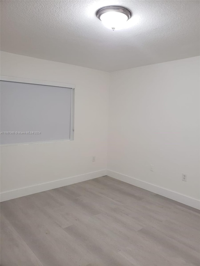 empty room featuring a textured ceiling, baseboards, and wood finished floors