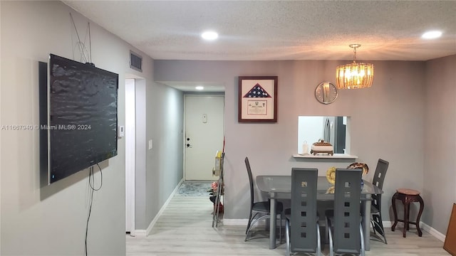 dining area with a textured ceiling, light hardwood / wood-style flooring, and a notable chandelier